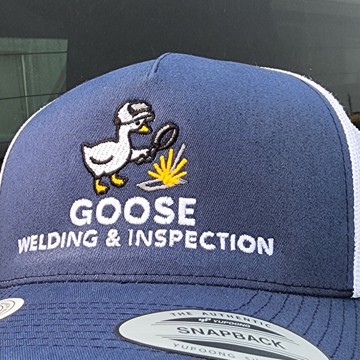 Multi-colour embroidered duck and welding spark logo with white lettering on a navy trucker cap