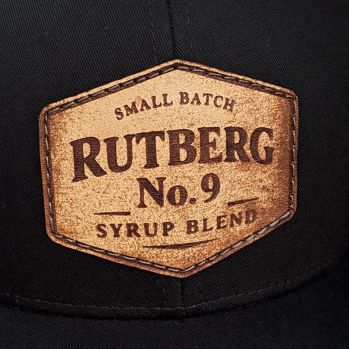 Hexagon leather patch with laser-engraved Small Batch Rutberg No. 9 Syrup Blend lettering on a black cap