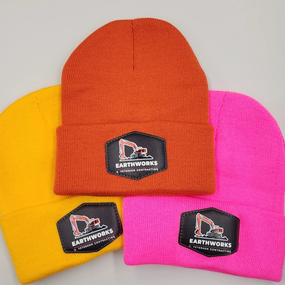 Yellow, orange and pink custom beanies with a printed Earthworks excavator logo patch