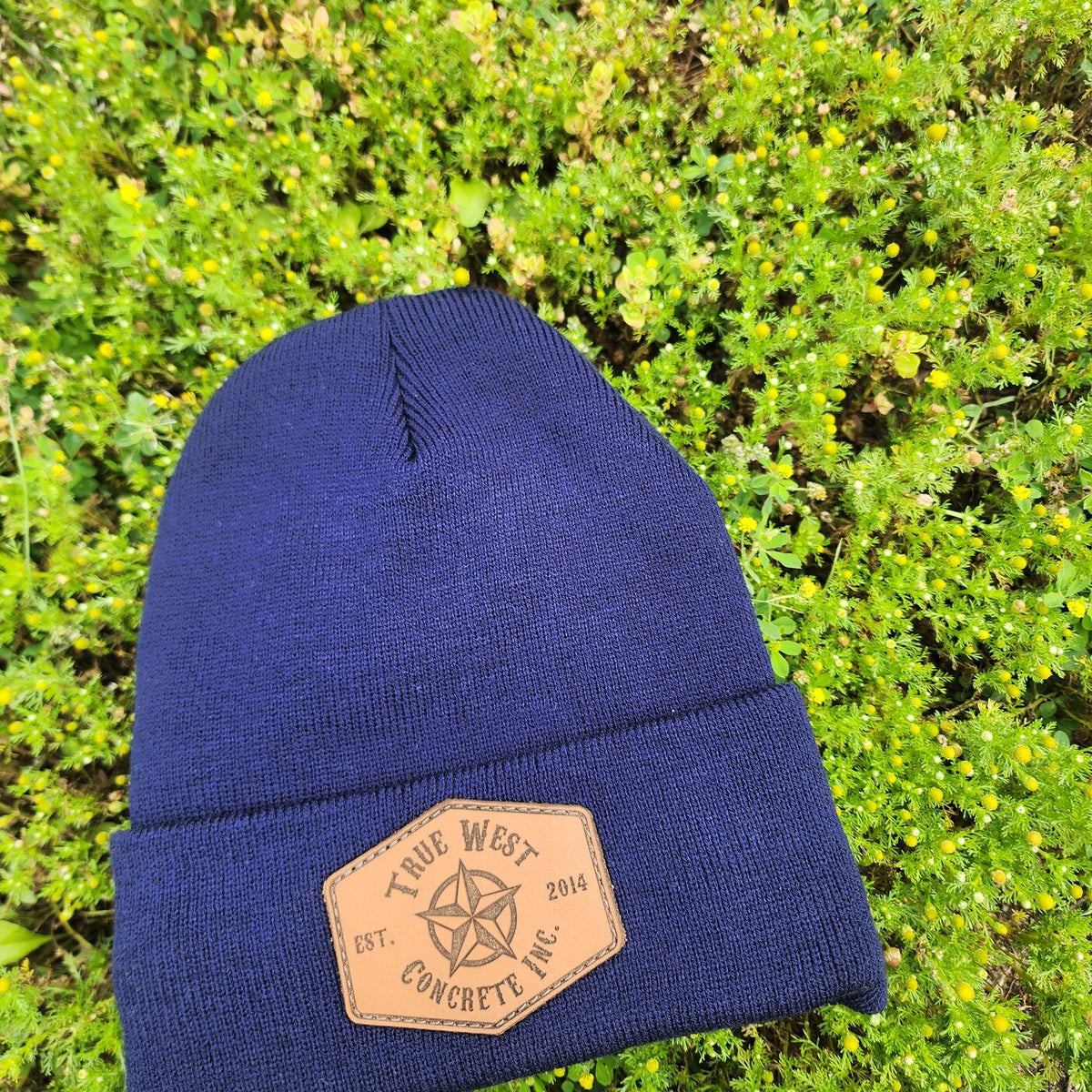 Navy custom toque with an engraved True West Concrete leather patch lying on green grass